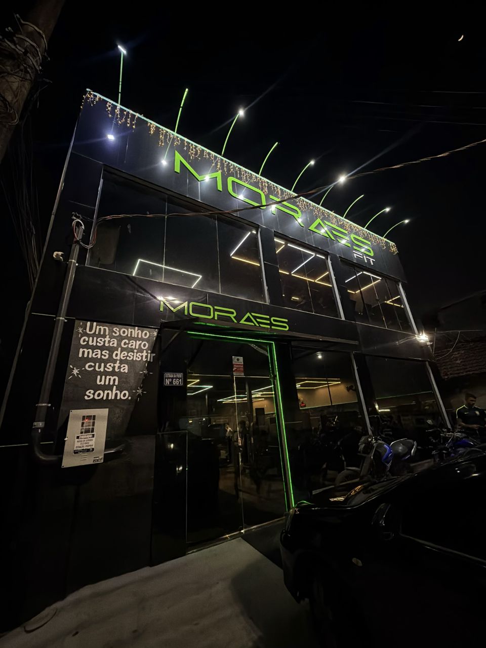 Fachada da Moraes Fit à noite, com o letreiro verde aceso