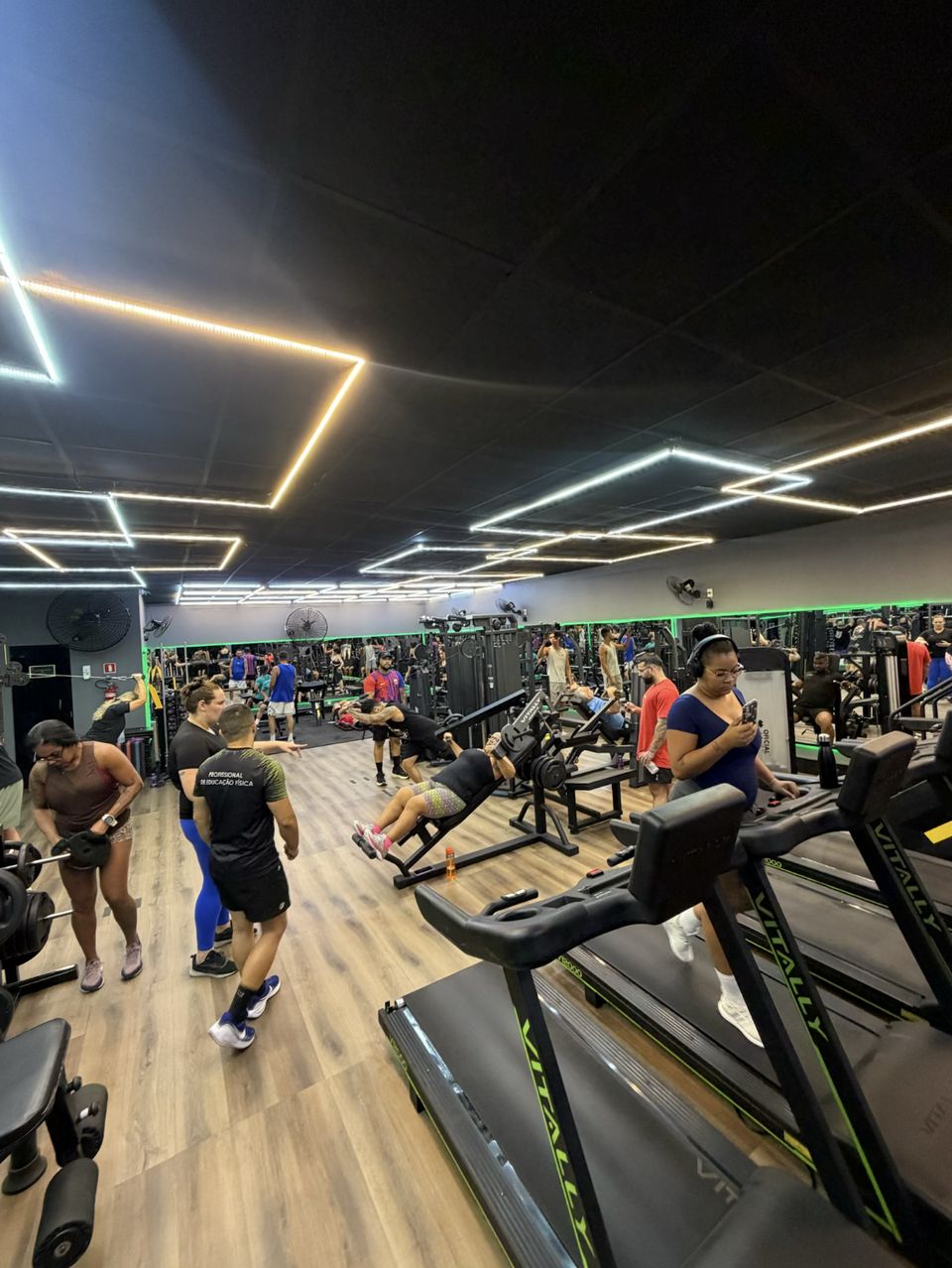 Sala de musculação da Moraes Fit cheia, com professor orientando alunos entre esteiras e aparelhos