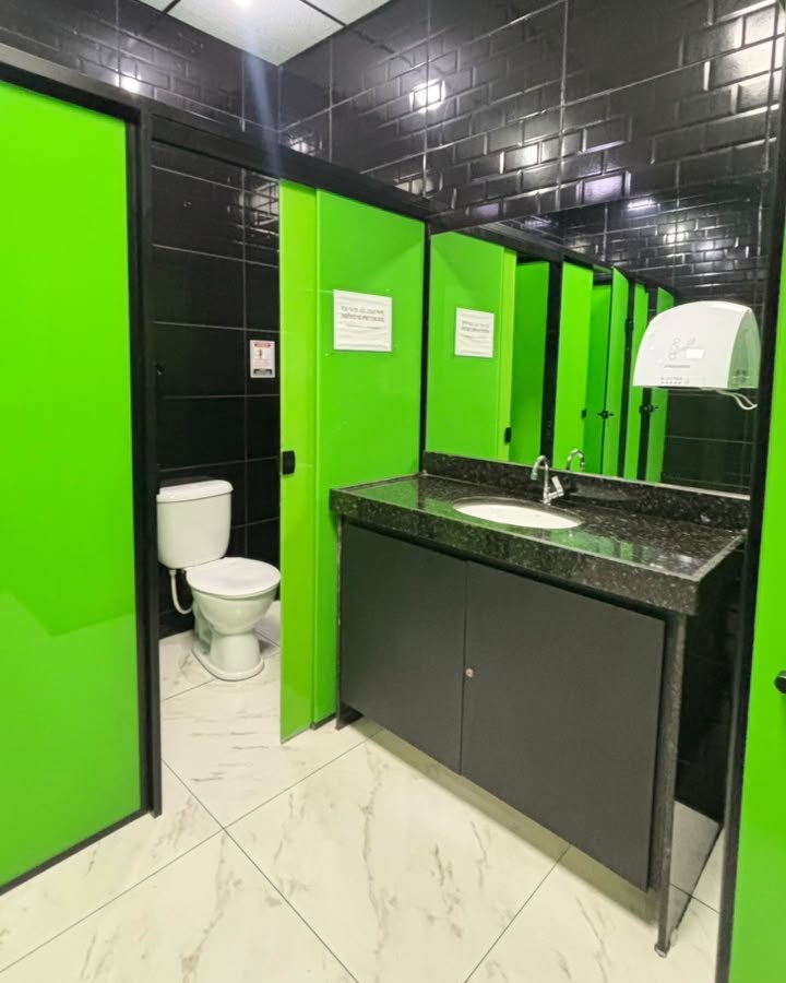 Banheiro da Moraes Fit com divisórias verdes, parede preta e pia de granito